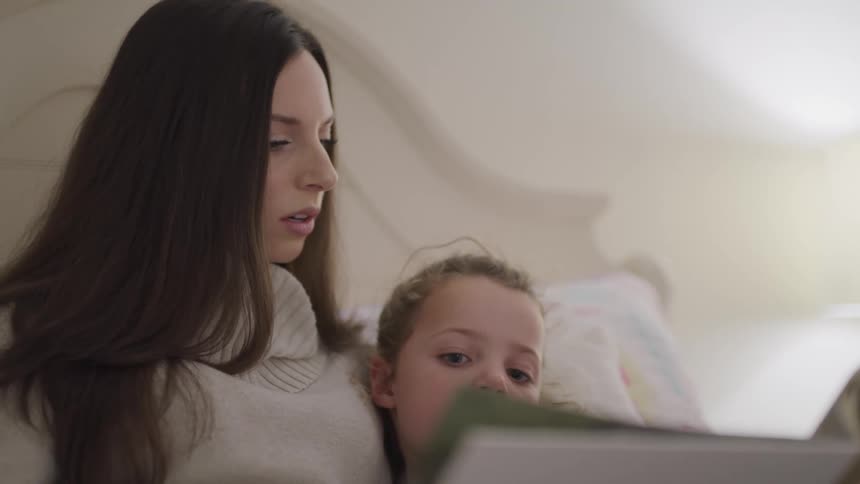 Woman wearing sweater reads book to daughter