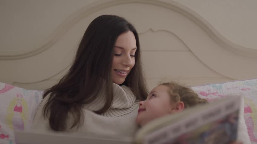 Mother reading to her daughter relaxing in bed