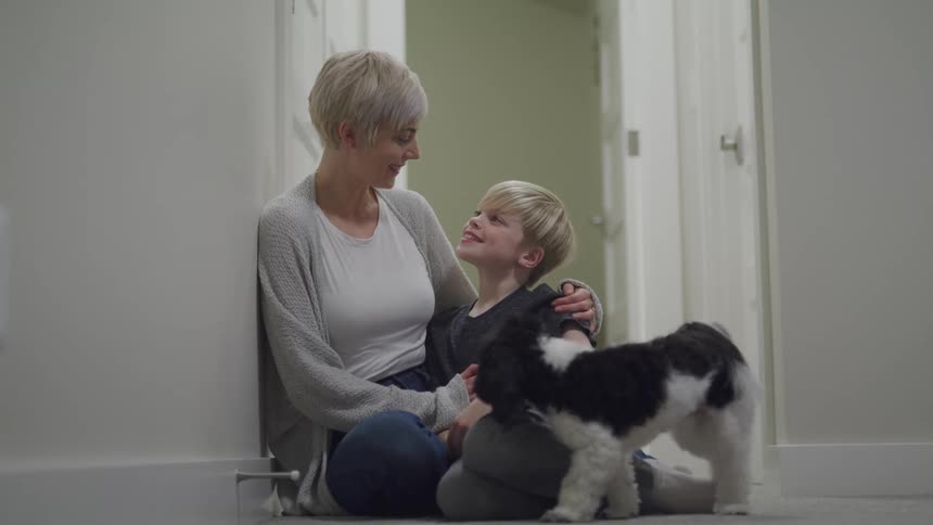 A mother sits on the floor at home with her son and while puppy walks around them