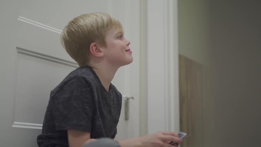 A young boy sits against a door and shuffles cards