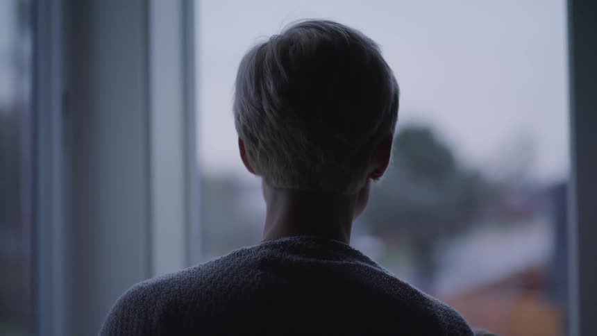 The silhouette of a woman is visible as she looks out of a large window