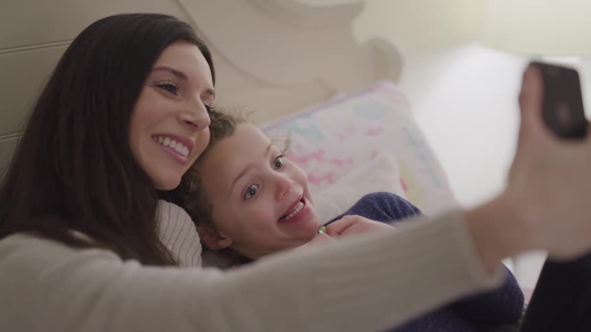 Mother and daughter taking a selfie while relaxing on the bed