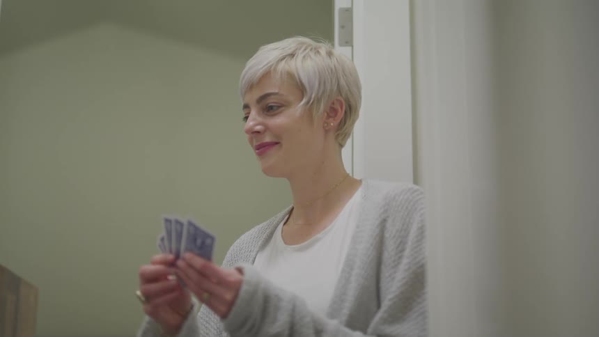 Woman with short blonde hair plays cards smilingly in a room