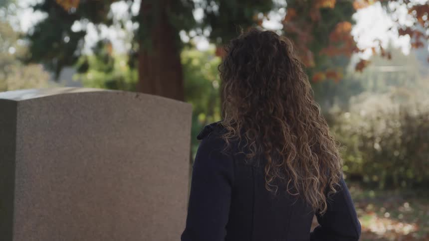 A young woman in a cemetery looks at a headstone