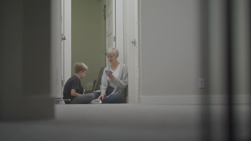 A woman and son sit in a hallway playing a card game