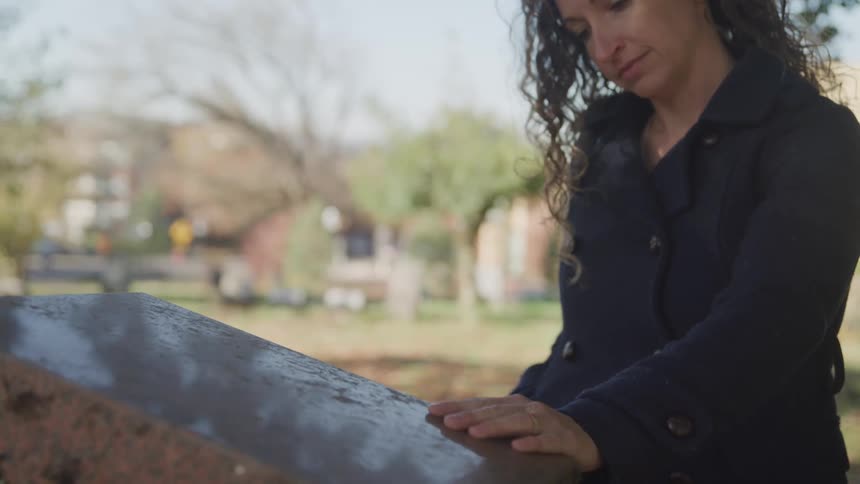 A woman touches a tombstone in the graveyard