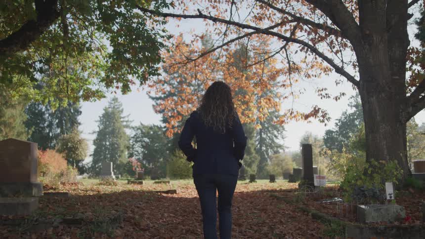 Woman walks through carpet of fallen leaves covering cemetery