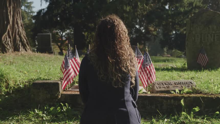 A woman sitting at a gravesite in a cemetery