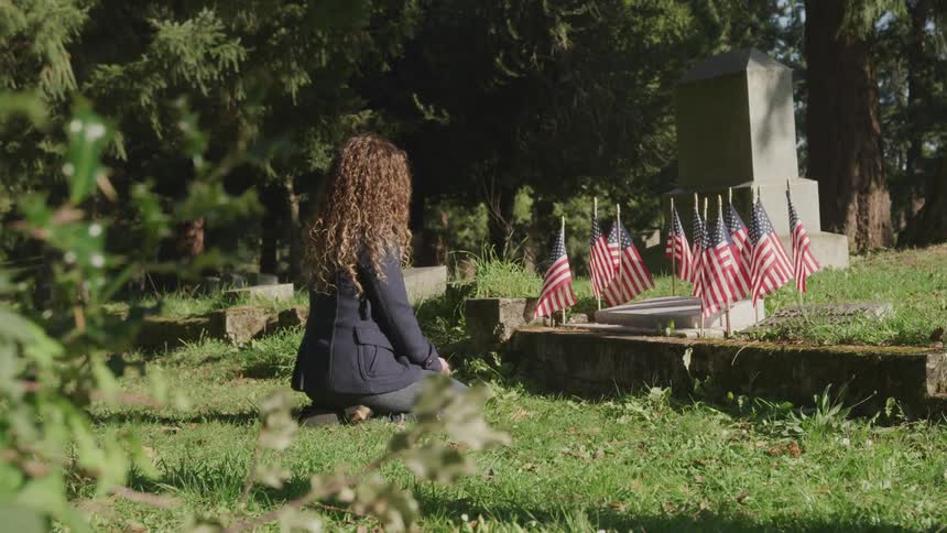A teenage girl is kneeling near a grave marker that is surrounded by headstones