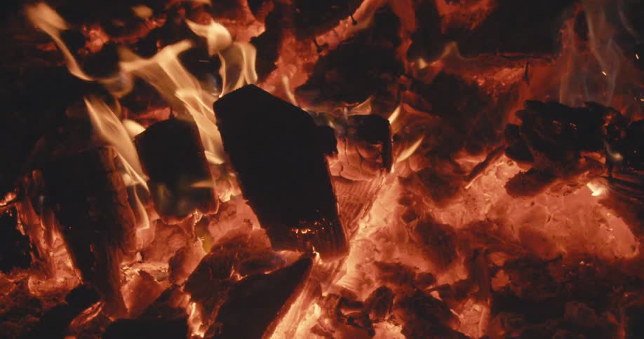Flames burn yellow against dark brown charred wood and orange embers