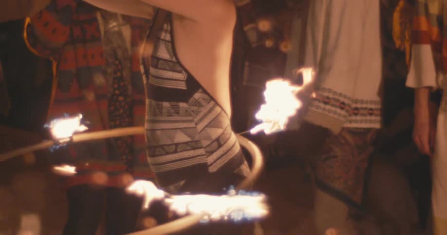 Woman in a black and white leotard fire dances with a hoop in front of a crowd at night