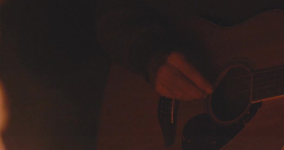 A man next to a fire playing the guitar in slomo