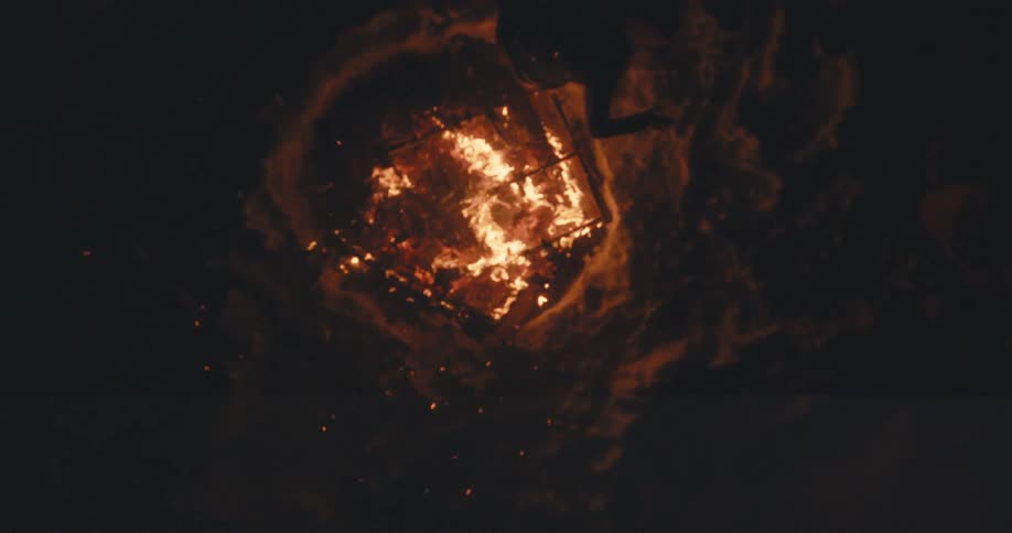 Overhead as a person jumps over a fire pit at night