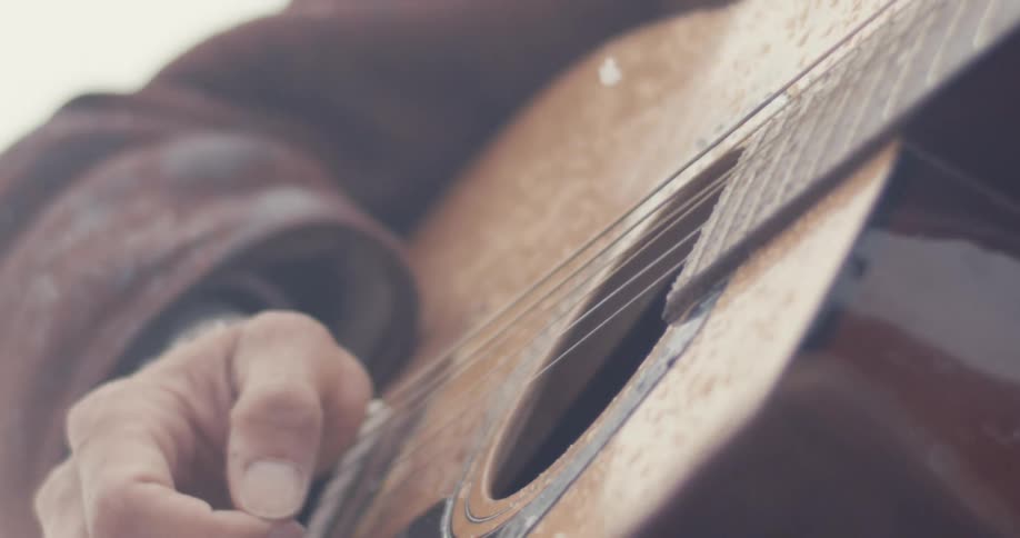 Man strums a guitar outside as it snows in macro