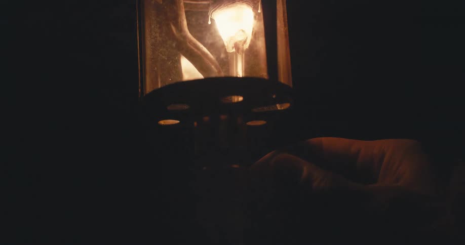 A hand turns off an old lantern in the darkness