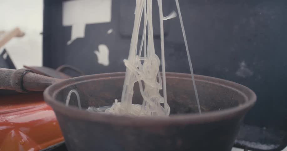 A person picking up noodles from a pan