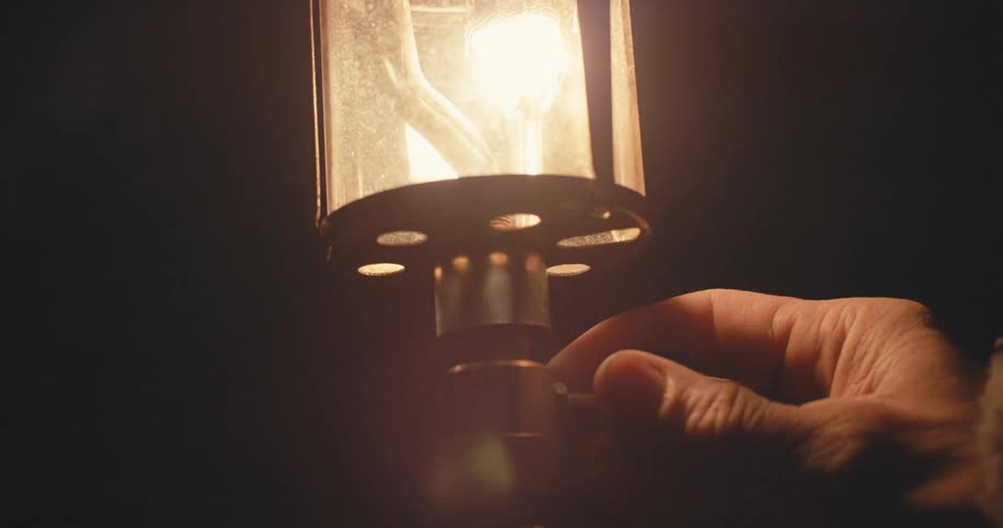 A person turning on a gas lantern in the dark