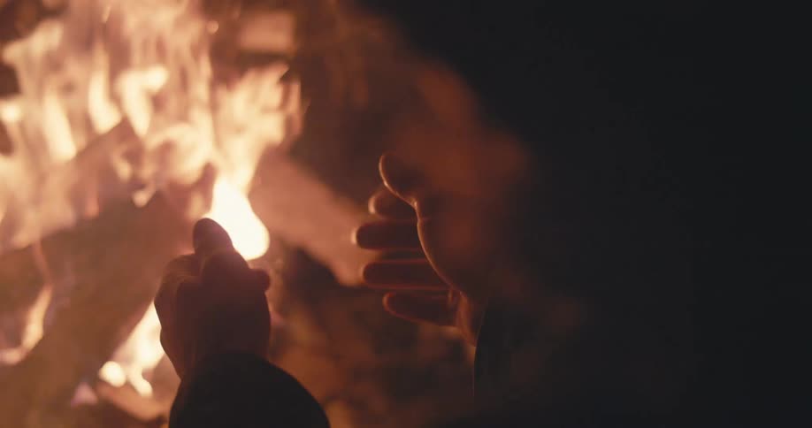 Man warms his hands by a campfire at night