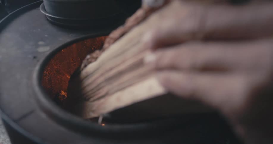 A man pushes a piece of firewood into a black metal stove