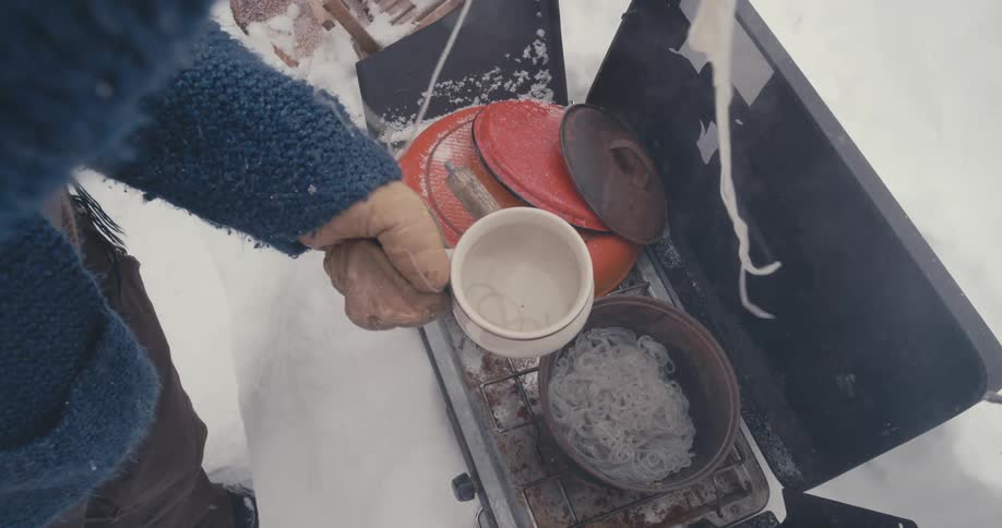 A woman cooking noodles outside in the snow
