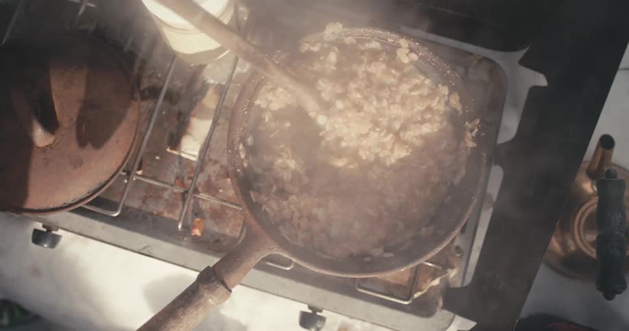 A person stirs a pot of oatmeal as it cooks on a stove top