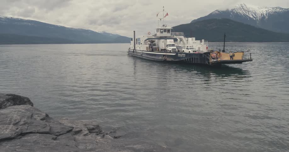A ferry carrying cars and trucks glides smoothly over the water with icy mountains around it