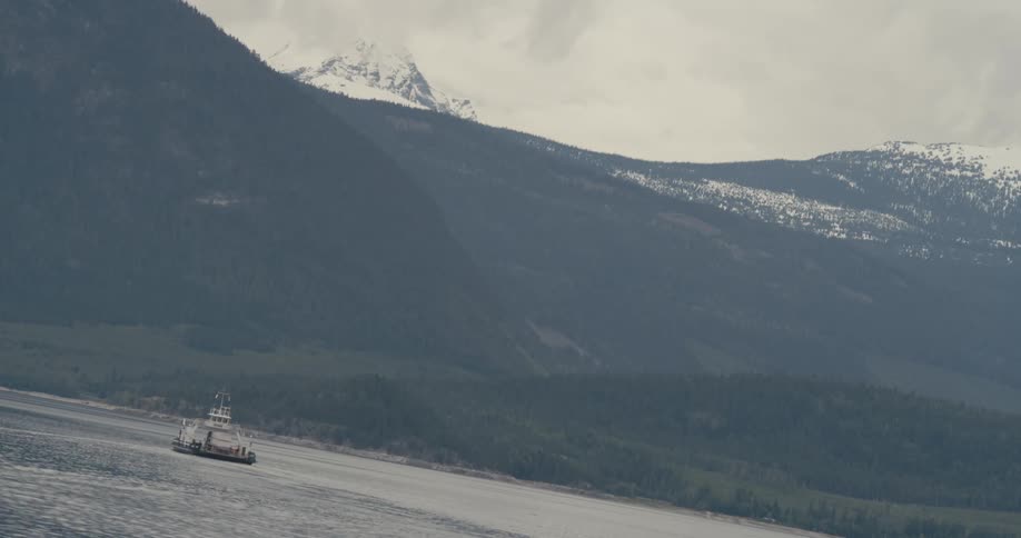 A boat crosses a lake in front of large mountain peaks
