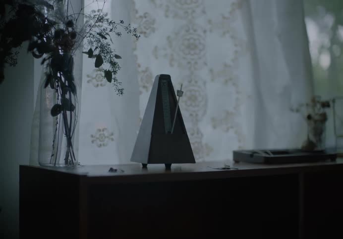 A metronome swings back and forth as it rests atop a shelf in front of a window in the living room of a house