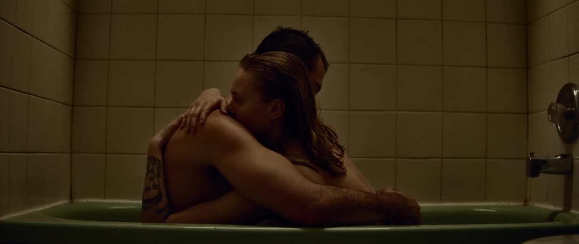 A man and woman sitting in a bathtub hugging one another