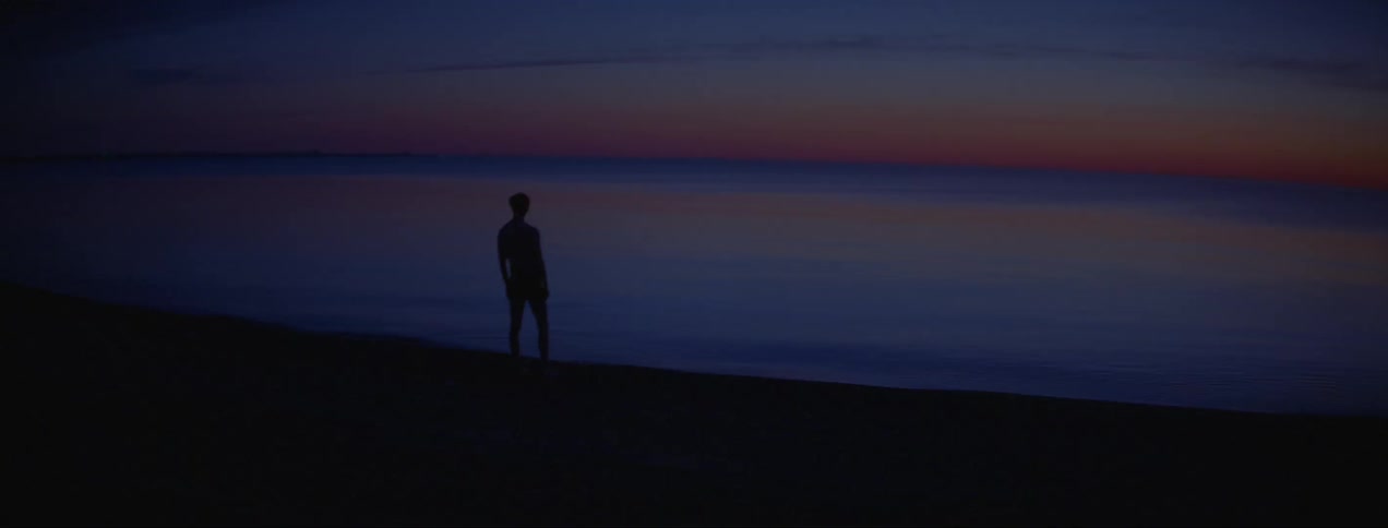 Silhouette of a young man standing in the shoreline of a beach at sunset