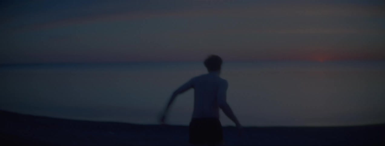 Shirtless young man screams and runs towards the coast and jumps in the sea water at sunset