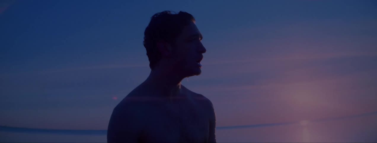 Soaking wet man stands in front of the shoreline of a beach at sunset
