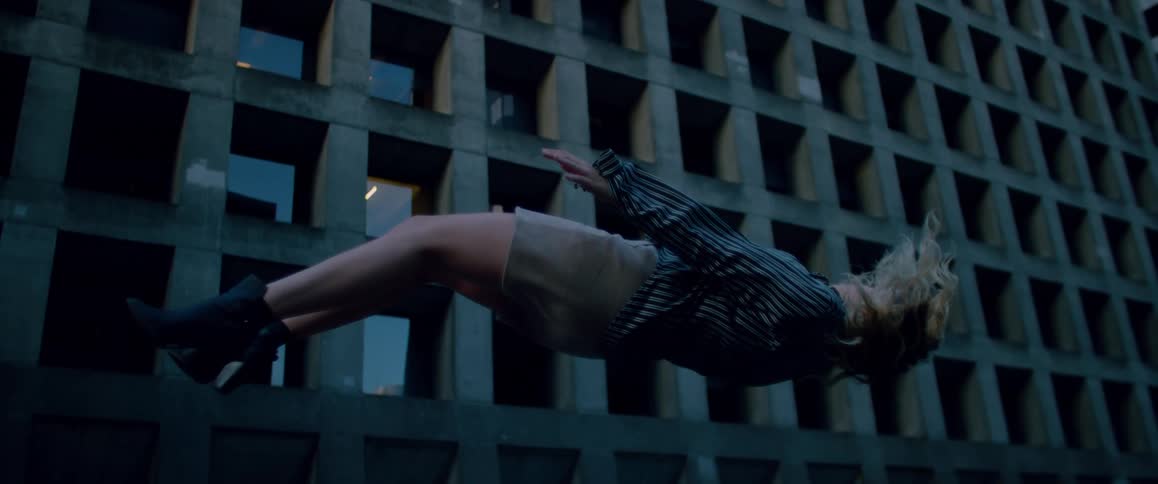 Blonde woman wearing a short skirt and a shirt floats in front of an office building