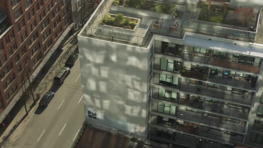 Sunlight reflects on the side of a city apartment building with a garden on the roof