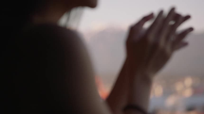 A white woman claps outdoors with a large city in the background