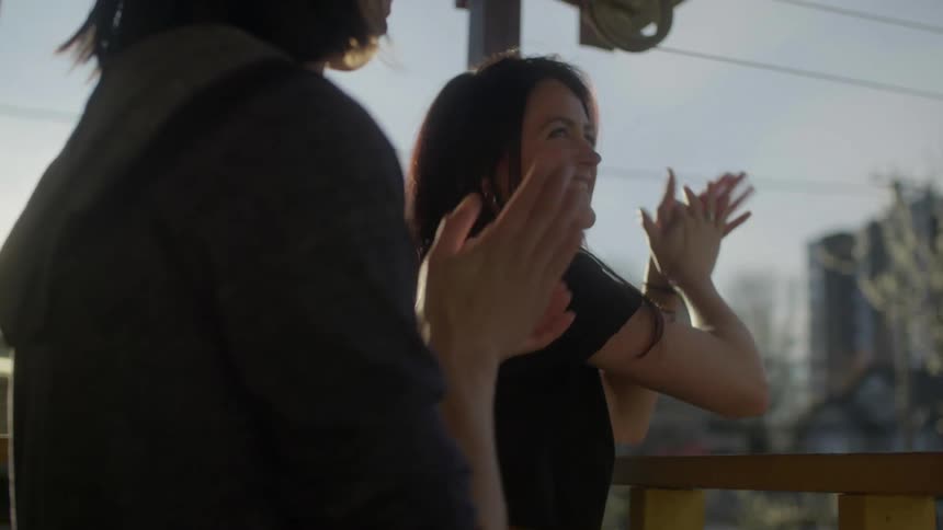 Woman and man clap their hands from balcony during the lockdown