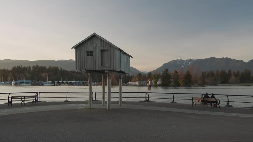 Two people sit on a bench by the water as someone else bikes past