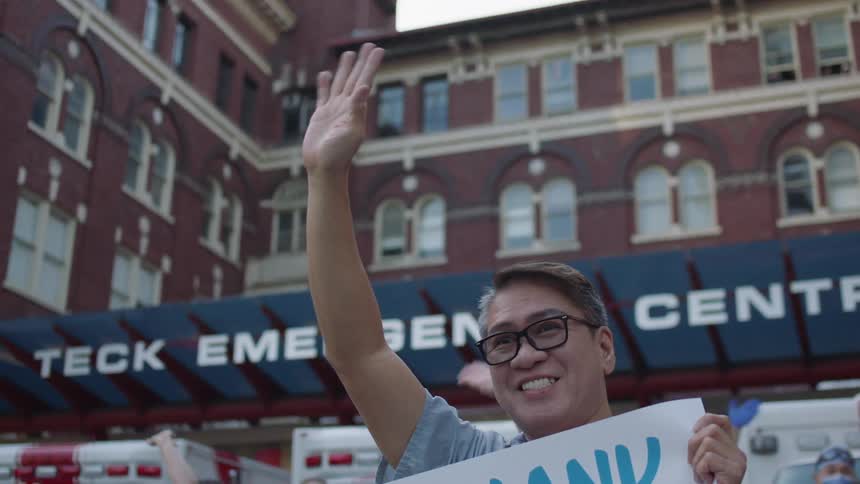 Medical workers wave while holding up signs in front of an emergency room