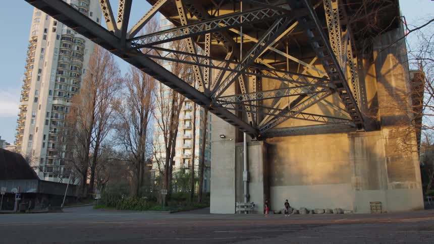 Two people play with a volleyball under a bridge overpass in a city on a sunny day