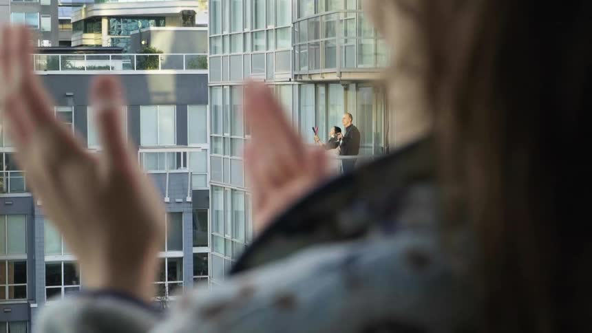 People standing on the balcony of their apartment clapping and banging on pots and pans
