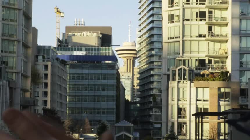 A person claps their hands on a city street with skyscrapers in the distance