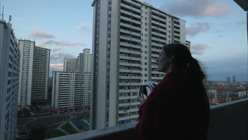 A woman stands on her balcony and bangs a spoon on to a pot