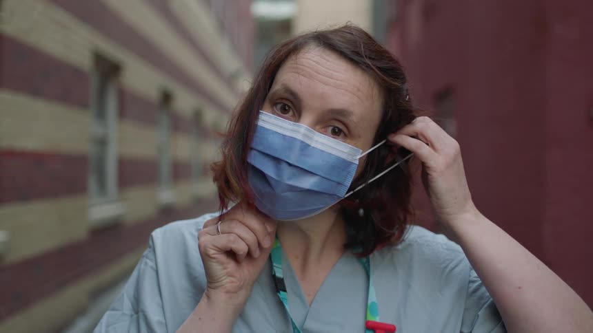 A nurse in scrubs puts on a blue surgical mask