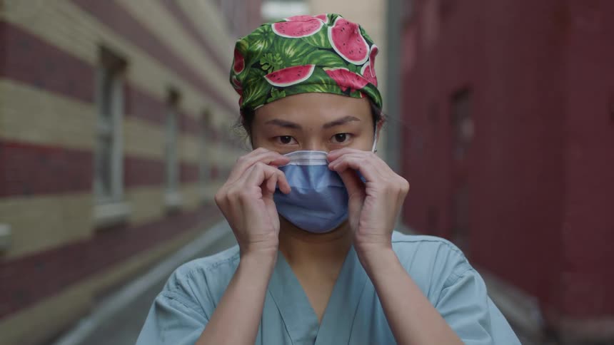 A female asian medical worker dons a face mask while standing outdoors