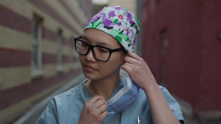 Female nurse takes off her face mask in the alley