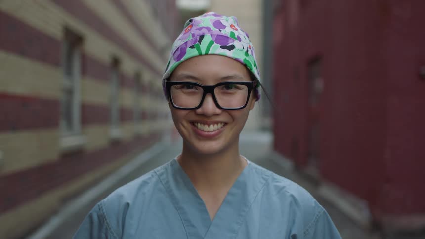 A woman dressed in scrubs stands outside and smiles