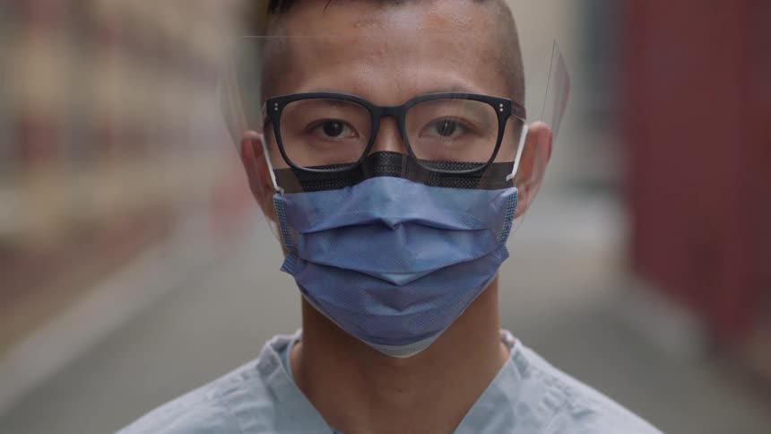 Asian male nurse wearing a face mask looks at the camera in the alley