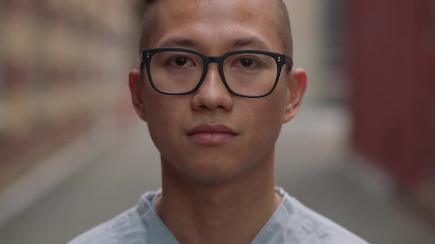 An asian man lifts his head up and looks forwards