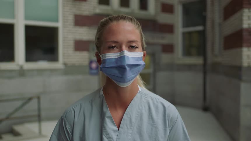 A woman with scrubs and a disposable mask standing