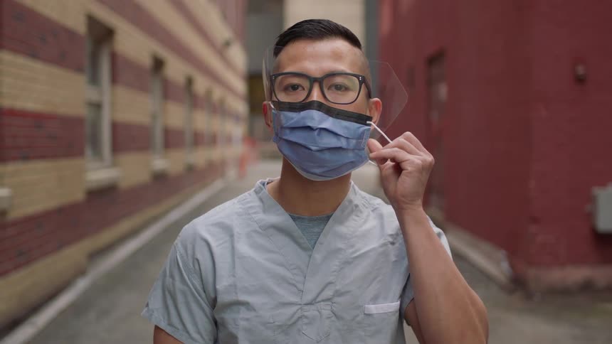 A man is standing outdoors and putting on a face mask